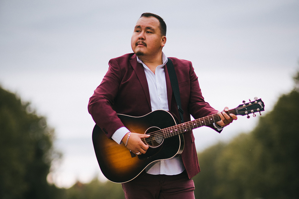 William Prince outdoors in burgundy suit jacket. 