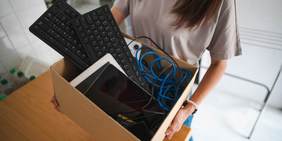 A person holding a box of keyboards and small electronic devices.