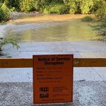 An orange barrier that blocks the entrance to a flooded trail.