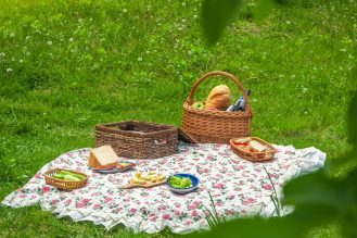 A picnic with food set up on the grass - including a picnic blanket and a basket