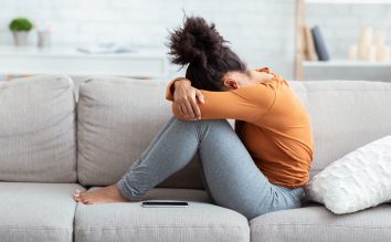 Woman sits on a couch with her head down on her knees