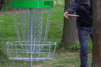 A person throwing a frisbee into a disc golf basket
