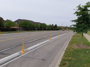 Photo of bike lane in street with yellow posts and cement curbs installed between lanes and street.