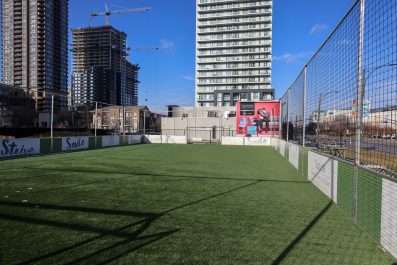 Boxed-in soccer field of green grass surrounded by tall buildings