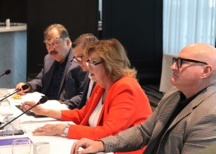 Mayor Parrish speaking into a microphone at a table alongside other members of her housing Task Force