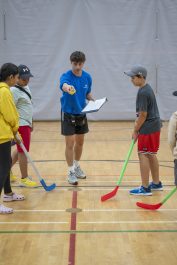 A group of youth gather for the opening face off in a gym ball hockey game.