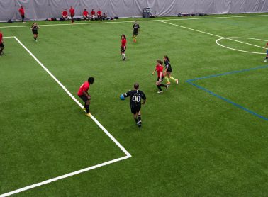 A group of soccer players pursue the ball at an indoor facility.