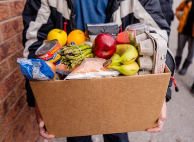 Person carrying box filled to the brim with food.