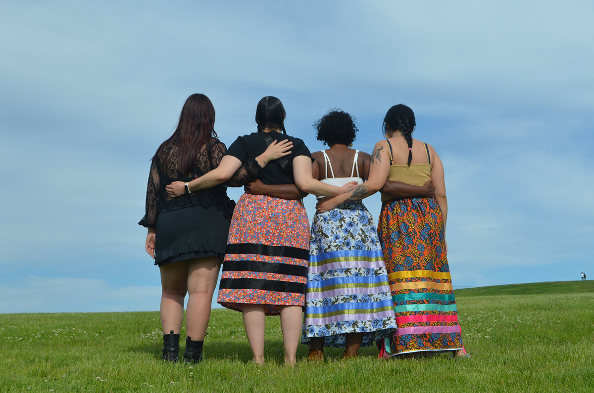 A group of women on grass with arms around each other's waist.