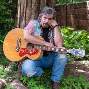 Chase Stevens kneeling holding a guitar.