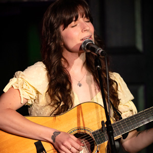 Adina Vlaslov singing while playing a guitar.