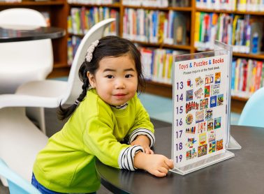 A child in a green shirt at a desk in a library.