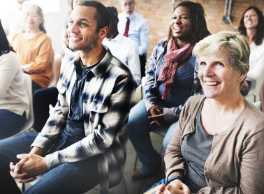 A group of people sit on foldout chairs looking attentive.