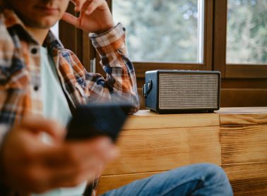 Young man sitting and relaxing, listening to music streams on his smartphone that is connected to a wireless speaker.