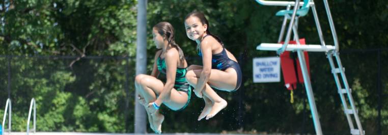 Girls jumping into an outdoor swimming pool
