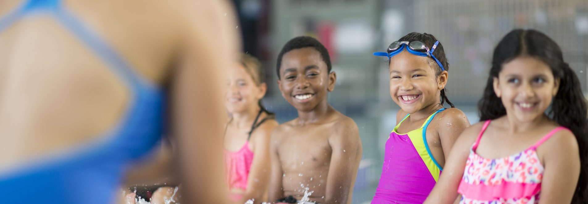 A multi-ethnic group of elementary age children are taking swimming lessons at the pool. They are splashing their feet in the water.